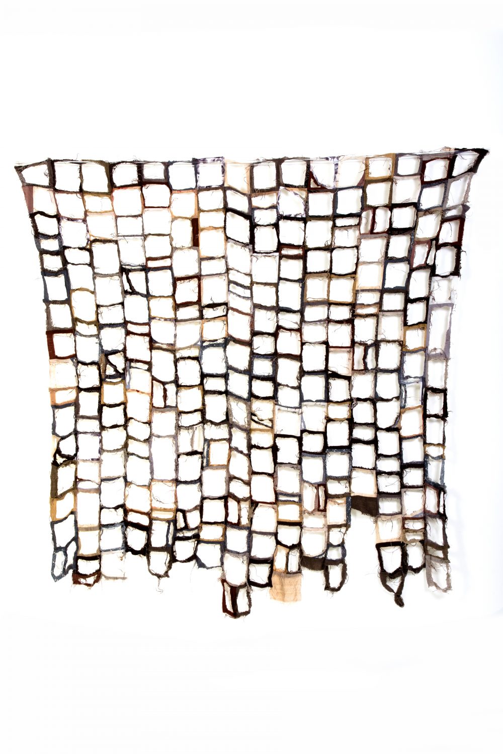 Quilt made from cloth in shades of brown with centres cut away from each small square, leaving seams only