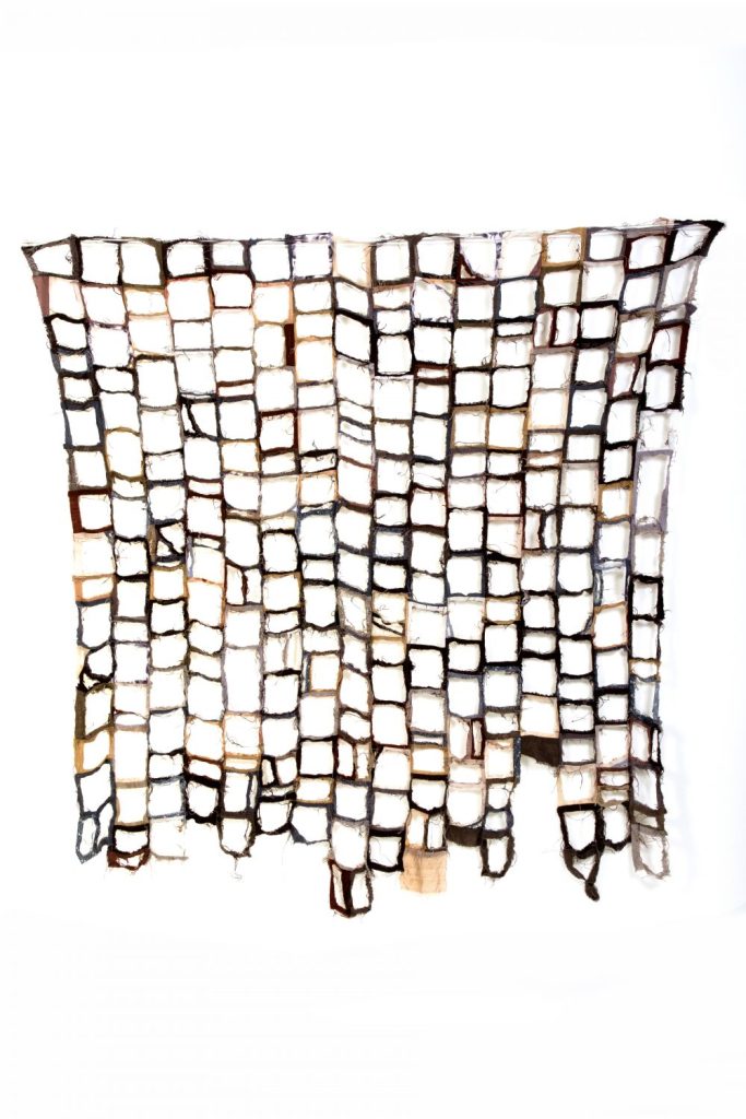 Quilt made from cloth in shades of brown with centres cut away from each small square, leaving seams only