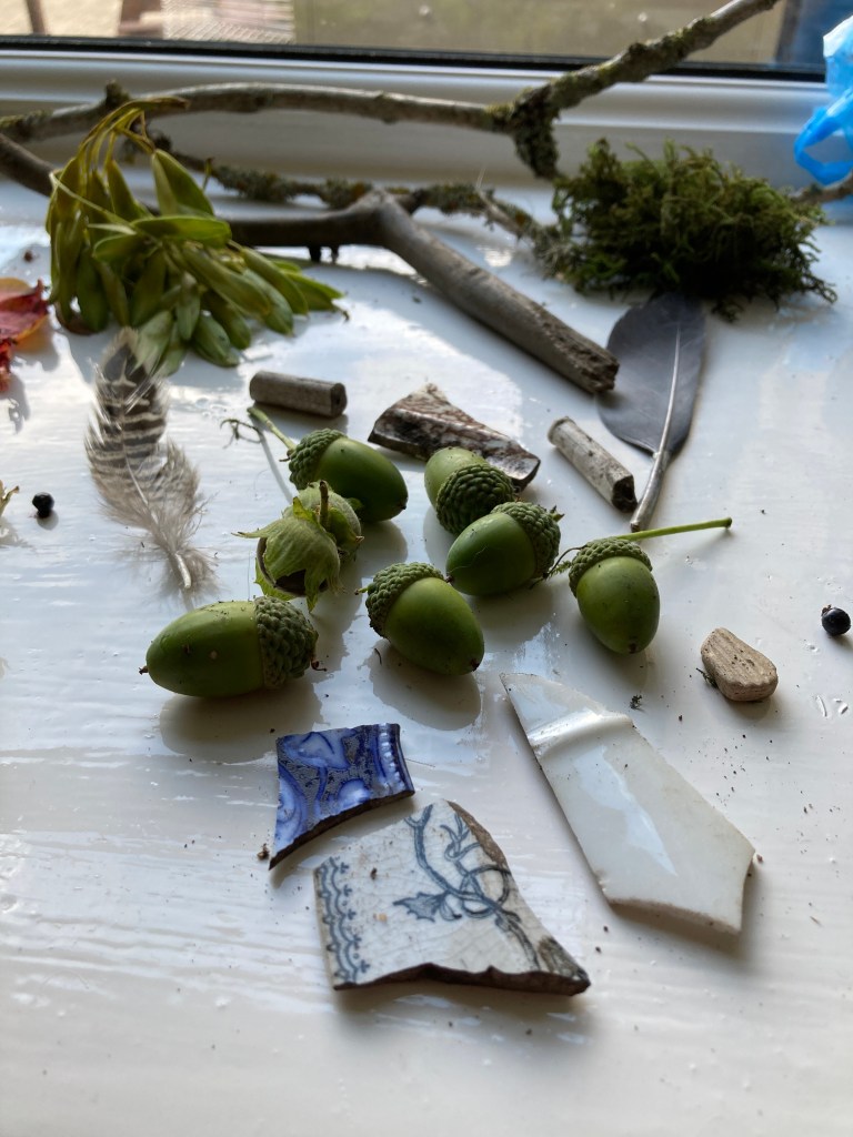 Collection of found objects and natural materials including acorns and old broken pottery, feathers and twigs